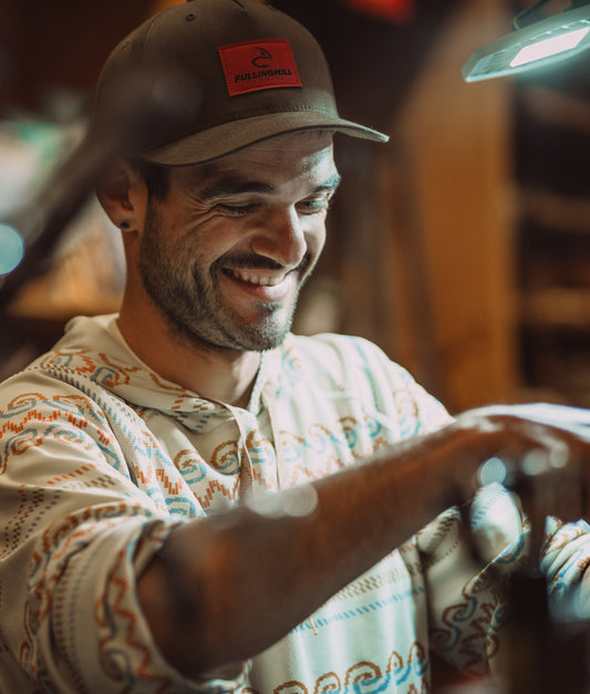 Man wearing a cap with a logo, smiling and working on something.